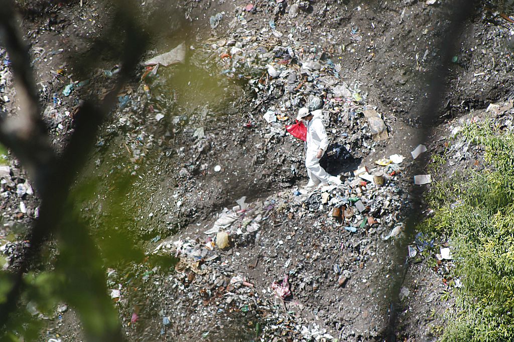 A forensic examiner searches for human remains below a garbage-strewn hillside in the densely forested mountains on the outskirts of Cocula, Mexico, on October 28, 2014. Suspects arrested earlier this week told prosecutors that many of the 43 students who disappeared on September 26 from Iguala had been held near this location. Mexico recoiled in fresh horror Tuesday over the discovery of yet another mass grave, in the futile month-long search for 43 missing college students. AFP PHOTO/ JESUS GUERRERO (Photo credit should read JESUS GUERRERO/AFP/Getty Images)