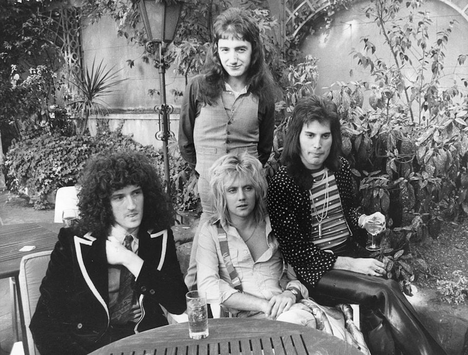 September 1976: British rock group Queen at Les Ambassadeurs, where they were presented with silver, gold and platinum discs for sales in excess of one million of their hit single 'Bohemian Rhapsody', which was No 1 for 9 weeks. The band are, from left to right; Brian May, John Deacon (standing), Roger Taylor and Freddie Mercury (Frederick Bulsara, 1946 - 1991). (Photo by Ian Tyas/Keystone/Getty Images)