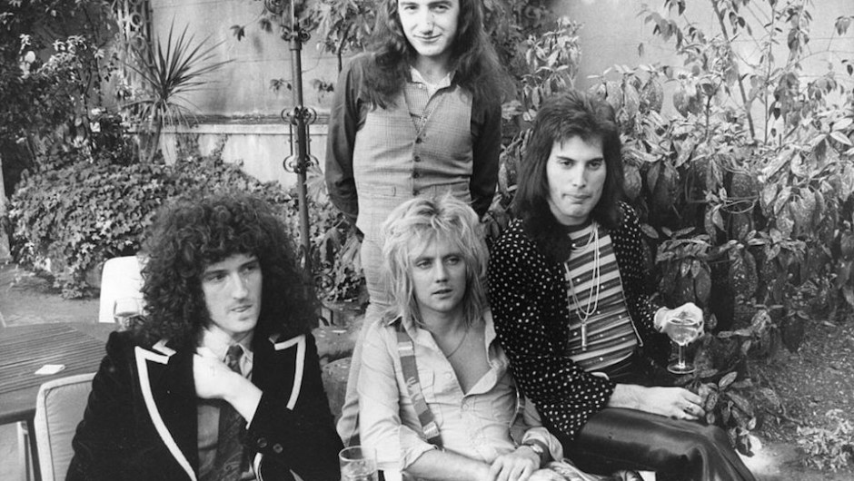 September 1976: British rock group Queen at Les Ambassadeurs, where they were presented with silver, gold and platinum discs for sales in excess of one million of their hit single 'Bohemian Rhapsody', which was No 1 for 9 weeks. The band are, from left to right; Brian May, John Deacon (standing), Roger Taylor and Freddie Mercury (Frederick Bulsara, 1946 - 1991). (Photo by Ian Tyas/Keystone/Getty Images)