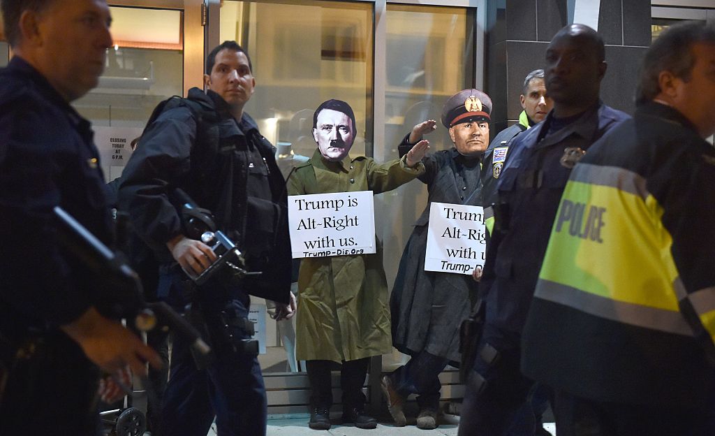 Dos hombres con máscaras de Adolfo Hitler y Benito Mussolini protestan en Washington haciendo el saludo nazi con carteles que dicen “Trump está de bien nosotros”, mientras policías vigilan la seguridad del lugar. (Crédito: PAUL J. RICHARDS/AFP/Getty Images)