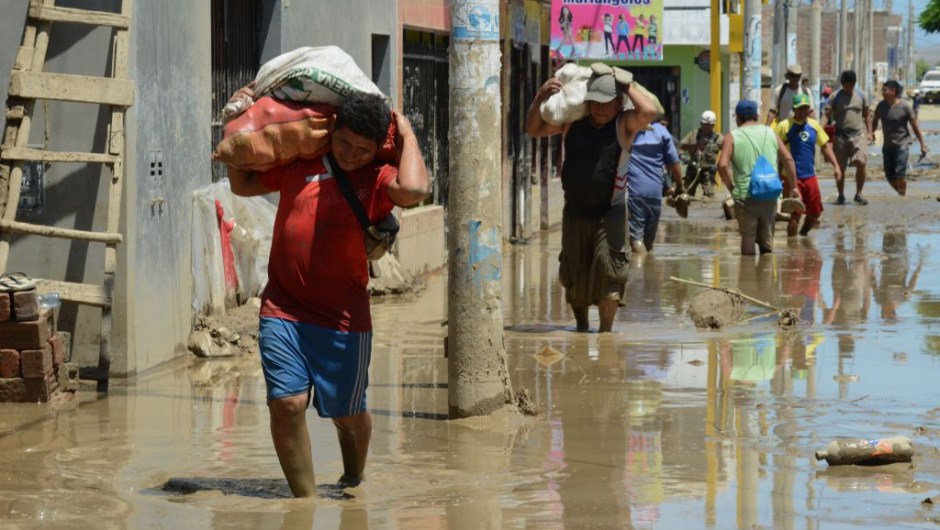 Local residents of the town of Huarmey, 300 kilometres north of Lima, wade through muddy water in the street on March 19, 2017 after a flash flood hit the evening before. The El Nino climate phenomenon is causing muddy rivers to overflow along the entire Peruvian coast, isolating communities and neighbourhoods. Thousands have been affected since January, and 72 people have died. Most cities face water shortages as water lines have been compromised by mud and debris. / AFP PHOTO / CRIS BOURONCLE (Photo credit should read CRIS BOURONCLE/AFP/Getty Images)