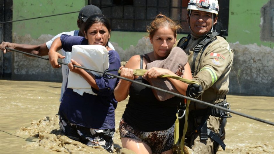 Rescuers help local residents of the town of Huarmey, 300 kilometres north of Lima, wade through muddy water in the street on March 19, 2017 after a flash flood hit the evening before. The El Nino climate phenomenon is causing muddy rivers to overflow along the entire Peruvian coast, isolating communities and neighbourhoods. Thousands have been affected since January, and 72 people have died. Most cities face water shortages as water lines have been compromised by mud and debris. / AFP PHOTO / CRIS BOURONCLE (Photo credit should read CRIS BOURONCLE/AFP/Getty Images)