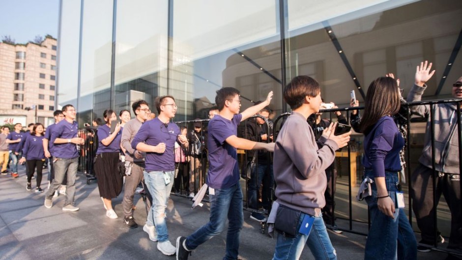 Apple employees (in blue) wave to Chinese customers as they queue up outside the Apple store to get their hands on the new iPhone X in Hangzhou in China's eastern Zhejiang province on November 3, 2017. Apple profits soared by a fifth as its flagship iPhone X hit stores in Asia on November 3, with the company predicting bumper sales despite its eye-watering price tag. / AFP PHOTO / STR / China OUT (Photo credit should read STR/AFP/Getty Images)