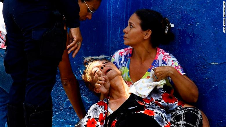 A woman is overcome by tear gas that was used to disperse the relatives of prisoners who were waiting to hear news about their family members imprisoned at a police station where a riot broke out, in Valencia, Venezuela, Wednesday, March 28, 2018. In a state police station housing more than one hundred prisoners, a riot culminated in a fire, requiring authorities to open a hole in a wall to rescue the inmates. (AP Photo/Juan Carlos Hernandez)