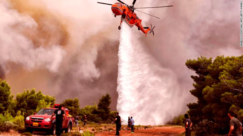 Un helicóptero de lucha contra incendios arroja agua para extinguir las llamas durante un incendio forestal en el pueblo de Kineta el martes.