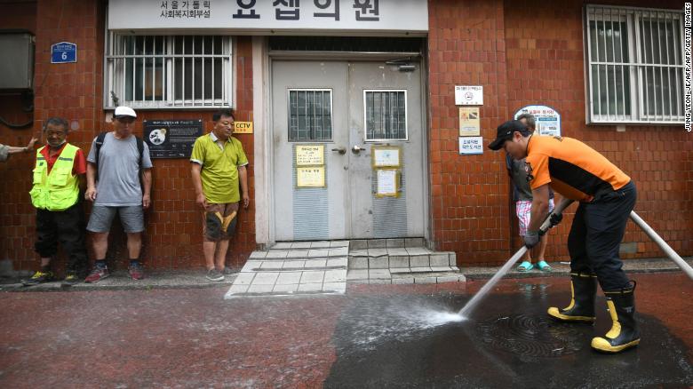 Un bombero echa agua en un callejón de un distrito residencial en Seúl para ayudar a aliviar el calor del verano.