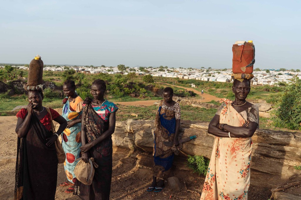 Las mujeres de Sudán del Sur esperan que otras se unan en el camino hacia el bosque para obtener leña. (Crédito: Hannah Reyes Morales)