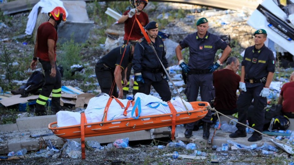 Rescuers and security forces watch as a recovered body in evacuated at the site where the Morandi motorway bridge collapsed in Genoa on August 14, 2018. - At least 30 people were killed on August 14 when the giant motorway bridge collapsed in Genoa in northwestern Italy. The collapse of the viaduct, which saw a vast stretch of the A10 freeway tumble on to railway lines in the northern port city, was the deadliest bridge failure in Italy for years, and the country's deputy transport minister warned the death toll could climb further. (Photo by Valery HACHE / AFP) (Photo credit should read VALERY HACHE/AFP/Getty Images)