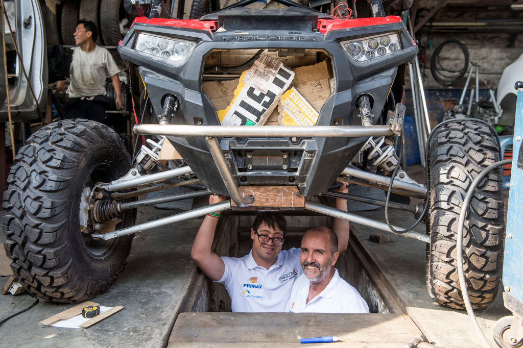 Jacques Barron (R) and his son and co-driver Lucas Barron, 25, pose under their UTV (Utility Task Vehicle) at a mechanics workshop in Lima, on December 18, 2018, where it is being prepared to take part in the upcoming Rally Dakar on January 2019. - Lucas Barron will make history on January 6 when he lines up on the Dakar 2019 start line in Peru, the first person with Down Syndrome to take part in the gruelling race. The 25-year-old, who will be co-pilot for his father Jacques, will tackle the world's most demanding rally: a 5,000 kilometer (3,000 miles), 10-day marathon, 70 percent of which will be raced over sand. (Photo by ERNESTO BENAVIDES / AFP) (Photo credit should read ERNESTO BENAVIDES/AFP/Getty Images)