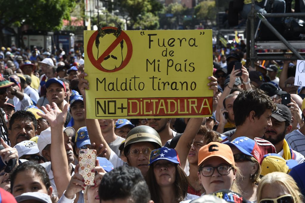 A supporter of Venezuelan opposition leader and self declared acting president Juan Guaido, displays a placard reading "Get Out of My Country, Damn Tyrant", "No More Dictatorship" , referring to President Nicolas Maduro, as people start gathering for a rally to press the military to let in US humanitarian aid, in eastern Caracas on February 12, 2019. - The tug of war between the government and opposition is centred on whether humanitarian aid will be allowed into the economically crippled country, which suffers shortages of food, medicine and other basics. (Photo by Federico PARRA / AFP) (Photo credit should read FEDERICO PARRA/AFP/Getty Images)