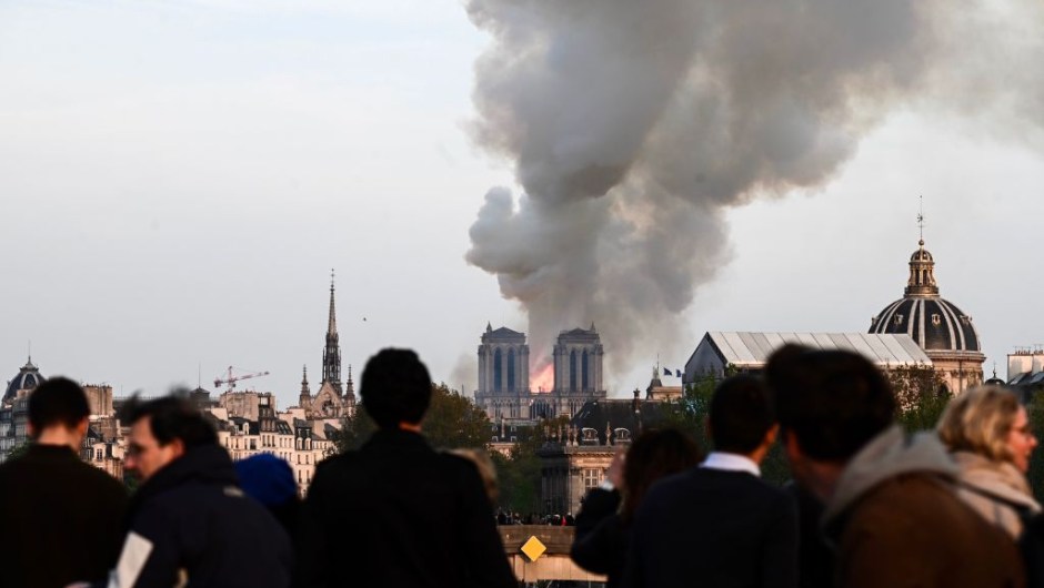 People watch the landmark Notre-Dame Cathedral burning in central Paris on April 15, 2019. - A huge fire swept through the roof of the famed Notre-Dame Cathedral in central Paris on April 15, 2019, sending flames and huge clouds of grey smoke billowing into the sky. The flames and smoke plumed from the spire and roof of the gothic cathedral, visited by millions of people a year. A spokesman for the cathedral told AFP that the wooden structure supporting the roof was being gutted by the blaze. (Photo by Philippe LOPEZ / AFP) (Photo credit should read PHILIPPE LOPEZ/AFP/Getty Images)