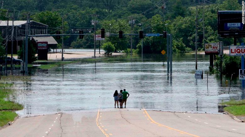 People stand in the middle of Rogers Avenue and look out over the flooded Massard Creek at the intersection of Meandering Way and Rogers Avenue, in Fort Smith, Ark., Saturday, May 25, 2019. (Jamie Mitchell/The Southwest Times Record via AP)