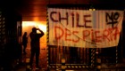 TOPSHOT - People take pictures of Macul Metro station set on fire by protesters alongside a sign that reads "Chile doesn't wake up" during a mass fare-dodging protest in Santiago, on October 19, 2019. - The entire Santiago Metro, which mobilizes about three million passengers per day, stopped operating on Friday afternoon following attacks in rejection of the rate hike, the company said. The chaos beat Santiago this Friday with confrontations, fires and attacks on the metropolitan railway, in protest of the increase in fares that forced the closure of all Metro stations. (Photo by JAVIER TORRES / AFP) (Photo by JAVIER TORRES/AFP via Getty Images)