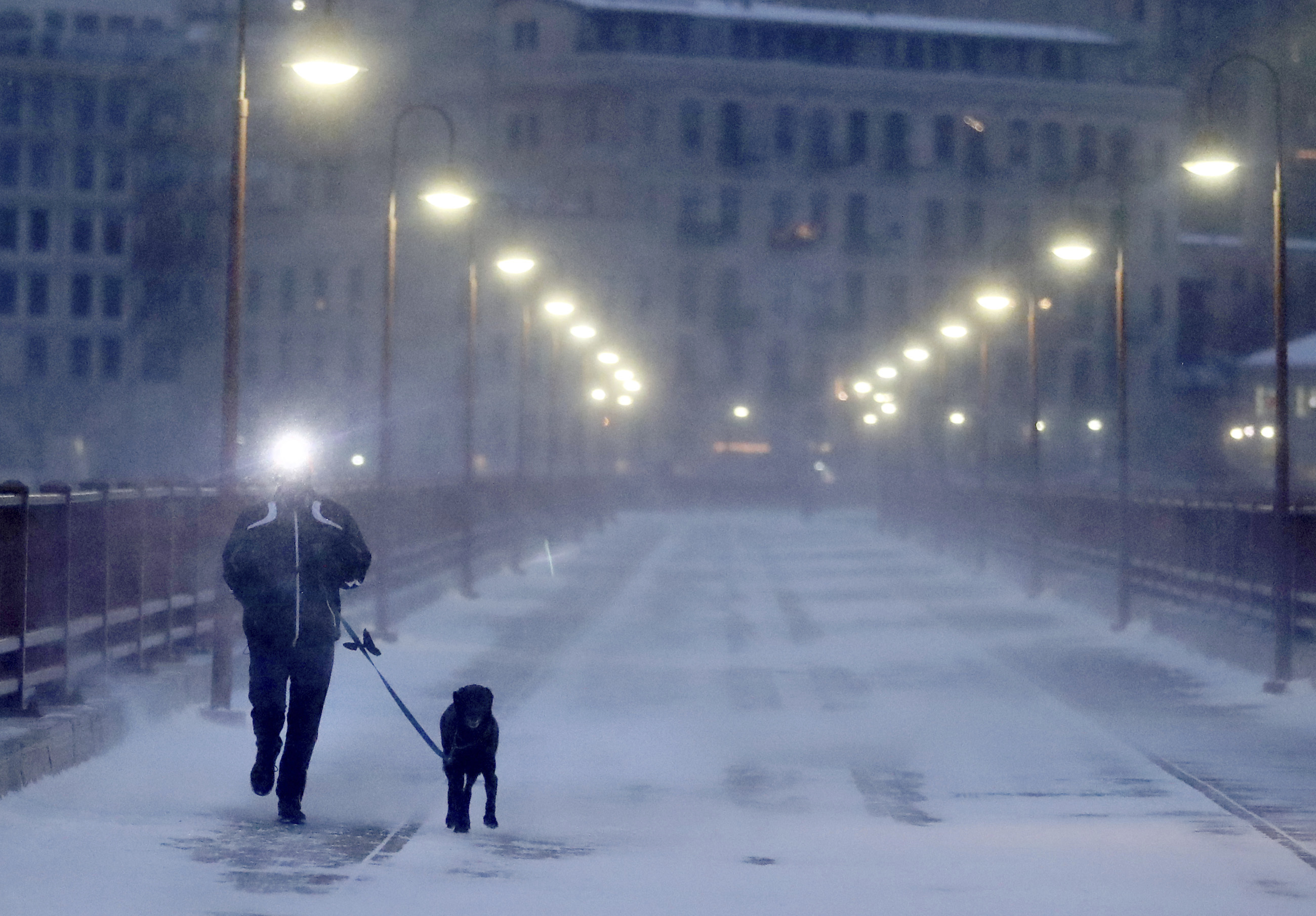 A runner and his dog brave frigid conditions while making their way east across the Stone Arch Bridge, Thursday, Jan. 24, 2019, in Minneapolis.   The National Weather Service issued a wind child advisory overnight Thursday for Wisconsin, Minnesota, the Dakotas and several other states. (David Joles/Star Tribune via AP)