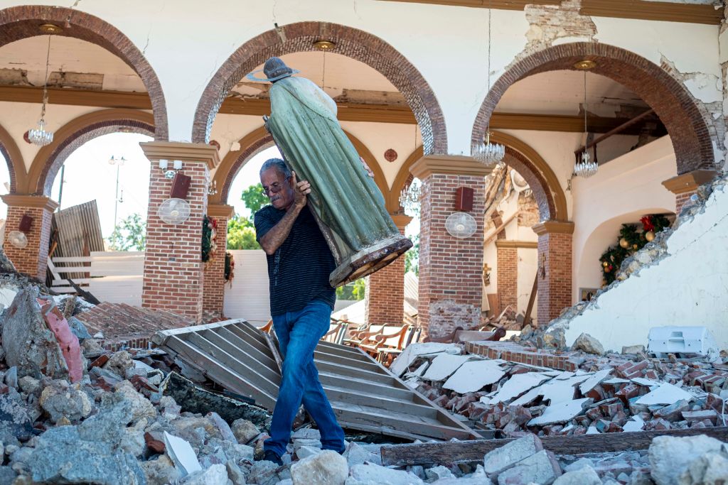 A man carries a St. Jude statue from the Inmaculada Concepcion church ruins that was built in 1841 and collapsed after an  earthquake hit the island in Guayanilla, Puerto Rico on January 7, 2020. - A strong earthquake struck south of Puerto Rico early January 7, 2020 followed by major aftershocks, the US Geological Survey said, the latest in a series of tremors that have shaken the island since December 28. The shallow 6.4 magnitude quake struck five miles (eight kilometers) south of the community of Indios, the USGS said, revising down its initial reading of 6.6. (Photo by Ricardo ARDUENGO / AFP) (Photo by RICARDO ARDUENGO/AFP via Getty Images)