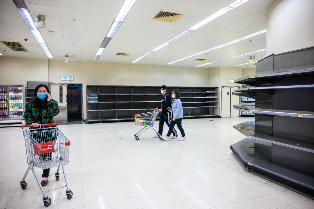 TOPSHOT - Shoppers wearing protective facemasks walk past bare supermarket shelves, usually stocked with toilet paper and kitchen rolls, in Hong Kong on February 6, 2020. - Panic buyers in Hong Kong have descended on supermarkets to snap up toilet paper after false online claims of shortages, prompting authorities to appeal for calm as the city's seven million residents fret about a deadly coronavirus outbreak. (Photo by Philip FONG / AFP) (Photo by PHILIP FONG/AFP via Getty Images)