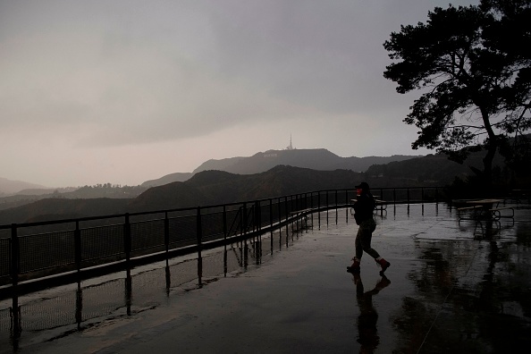 A person wears a face mask while walking to take pictures from a viewing area overlooking the Hollywood sign shrouded by clouds during heavy rains as seen from the Griffith Observatory on December 28, 2020 in Los Angeles, California. - Los Angeles residents woke up to rain today as the first major storm of the season hit the area. (Photo by Patrick T. Fallon / AFP) (Photo by PATRICK T. FALLON/AFP via Getty Images)