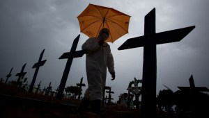 TOPSHOT - A worker wearing a protective suit and carrying an umbrella walks past the graves of COVID-19 victims at the Nossa Senhora Aparecida cemetery, in Manaus, Brazil, on February 25, 2021. - Brazil surpassed 250,000 deaths due to COVID-19. (Photo by MICHAEL DANTAS / AFP) (Photo by MICHAEL DANTAS/AFP via Getty Images)