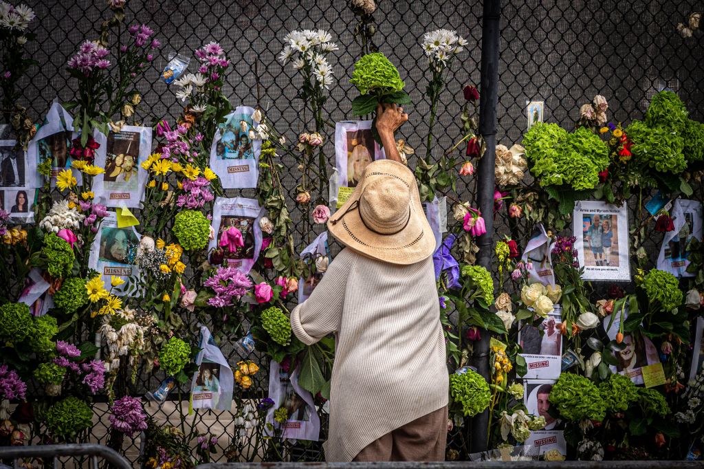 TOPSHOT - A woman adds flowers to a memorial featuring photos of some of those lost in the partially collapsed 12-story Champlain Towers South building on June 28, 2021 in Surfside, Florida. - Questions mounted Monday about how a residential building in the Miami area could have collapsed so quickly and violently last week, as the death toll rose to 11 with 150 still unaccounted for, and desperate families feared the worst. (Photo by Giorgio Viera / AFP) (Photo by GIORGIO VIERA/AFP via Getty Images)