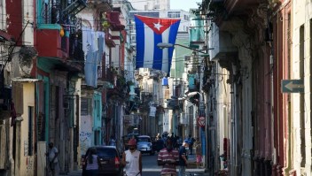 People walk along a street under a Cuban flag, in Havana, on October 14, 2021. (Photo by YAMIL LAGE / AFP) (Photo by YAMIL LAGE/AFP via Getty Images)