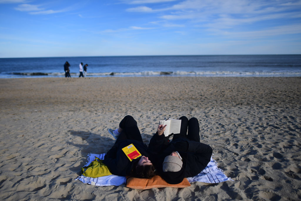 REHOBOTH BEACH, DE - JANUARY 2: A couple read books by the ocean on an unseasonably warm day on January 2, 2021 in Rehoboth Beach, Delaware. Due to the coronavirus (COVID-19) pandemic, face masks are required on the boardwalk and strongly recommended on the beach. (Photo by Mark Makela/Getty Images)