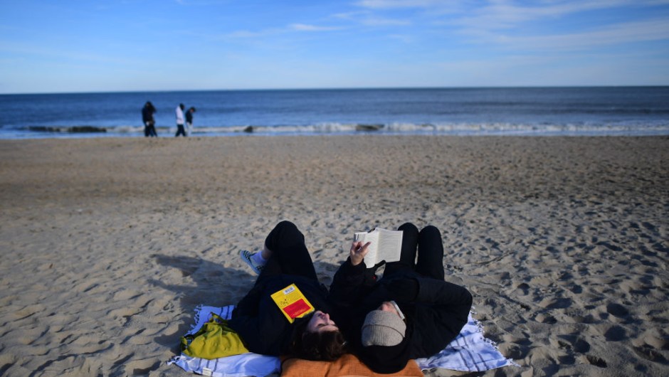 REHOBOTH BEACH, DE - JANUARY 2: A couple read books by the ocean on an unseasonably warm day on January 2, 2021 in Rehoboth Beach, Delaware. Due to the coronavirus (COVID-19) pandemic, face masks are required on the boardwalk and strongly recommended on the beach. (Photo by Mark Makela/Getty Images)