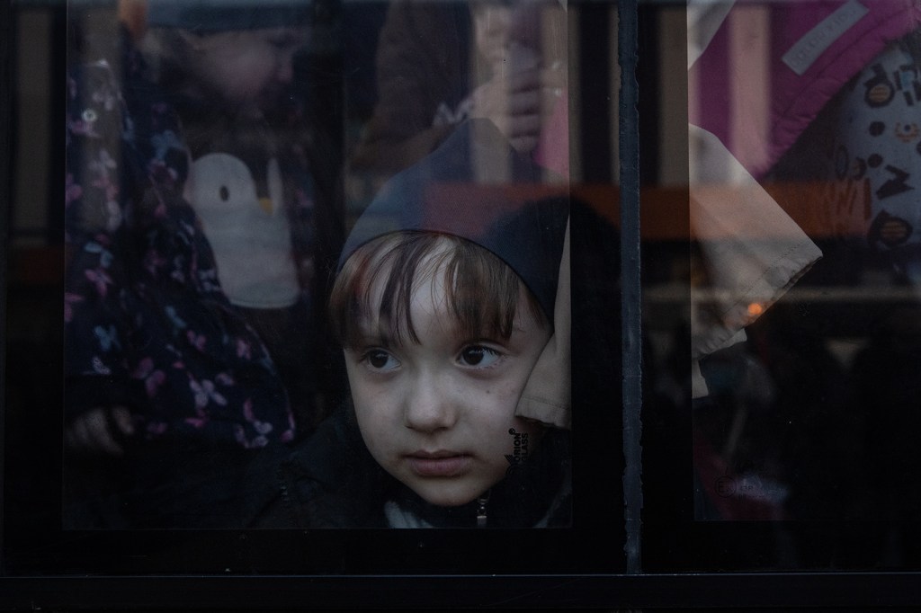 Un niño mira por la ventana de un autobús después de que un gran convoy de vehículos y autobuses llegara a un punto de evacuación, llevando a cientos de personas evacuadas de Mariúpol y Melitopol el 25 de marzo, en Zaporiyia, Ucrania. (Foto de Chris McGrath/Getty Images)
