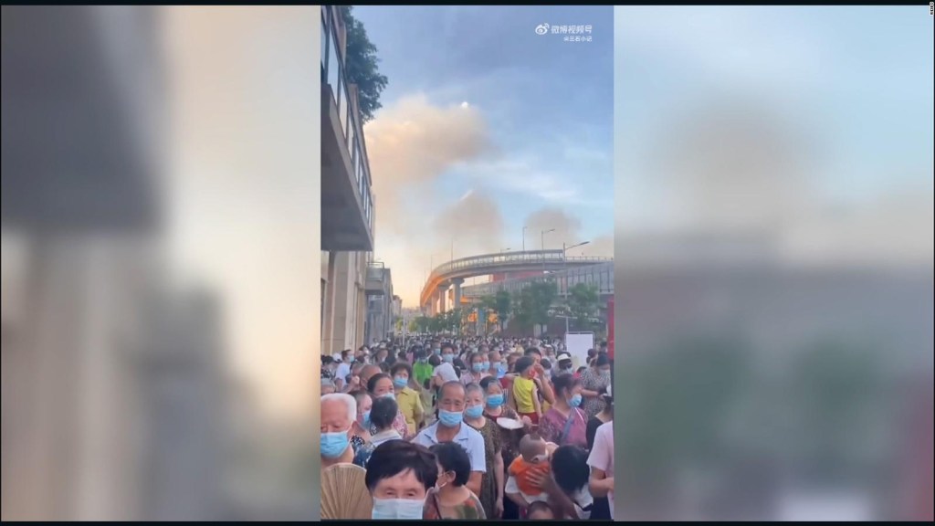 Residentes hacen fila para someterse a las pruebas obligatorias de covid en la ciudad china de Chongqing, mientras las columnas de humo de los incendios forestales se elevan en el fondo.