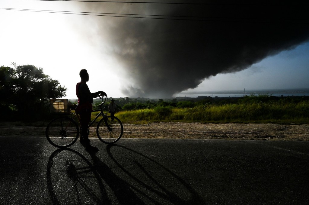 Un hombre en su bicicleta mira el humo negro del enorme incendio en un depósito de combustible en Matanzas, Cuba, el 9 de agosto de 2022.
