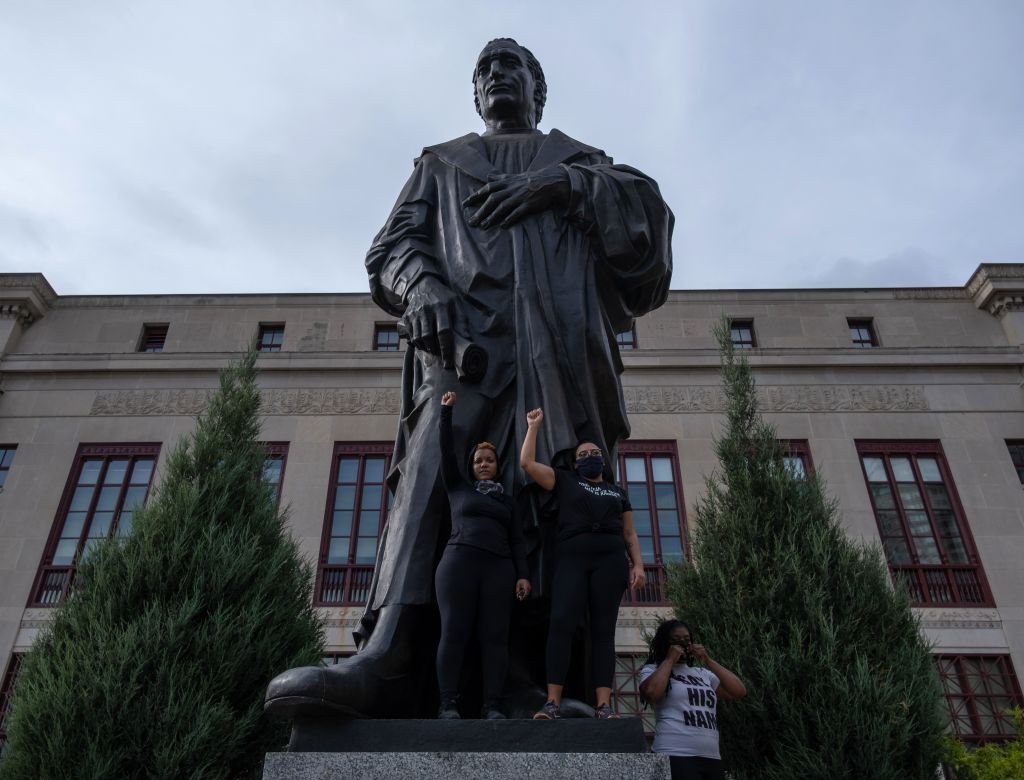 Los manifestantes levantan los puños en la base de una estatua de Cristóbal Colón frente al Ayuntamiento durante una protesta de Black Lives Matters contra la brutalidad policial en el centro de Columbus, Ohio, el 27 de junio de 2020 