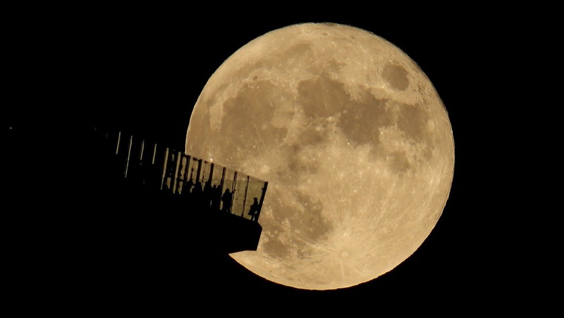 Personas en la plataforma de observación Edge NYC en la ciudad de Nueva York mientras sale la luna llena el 20 de octubre de 2021.