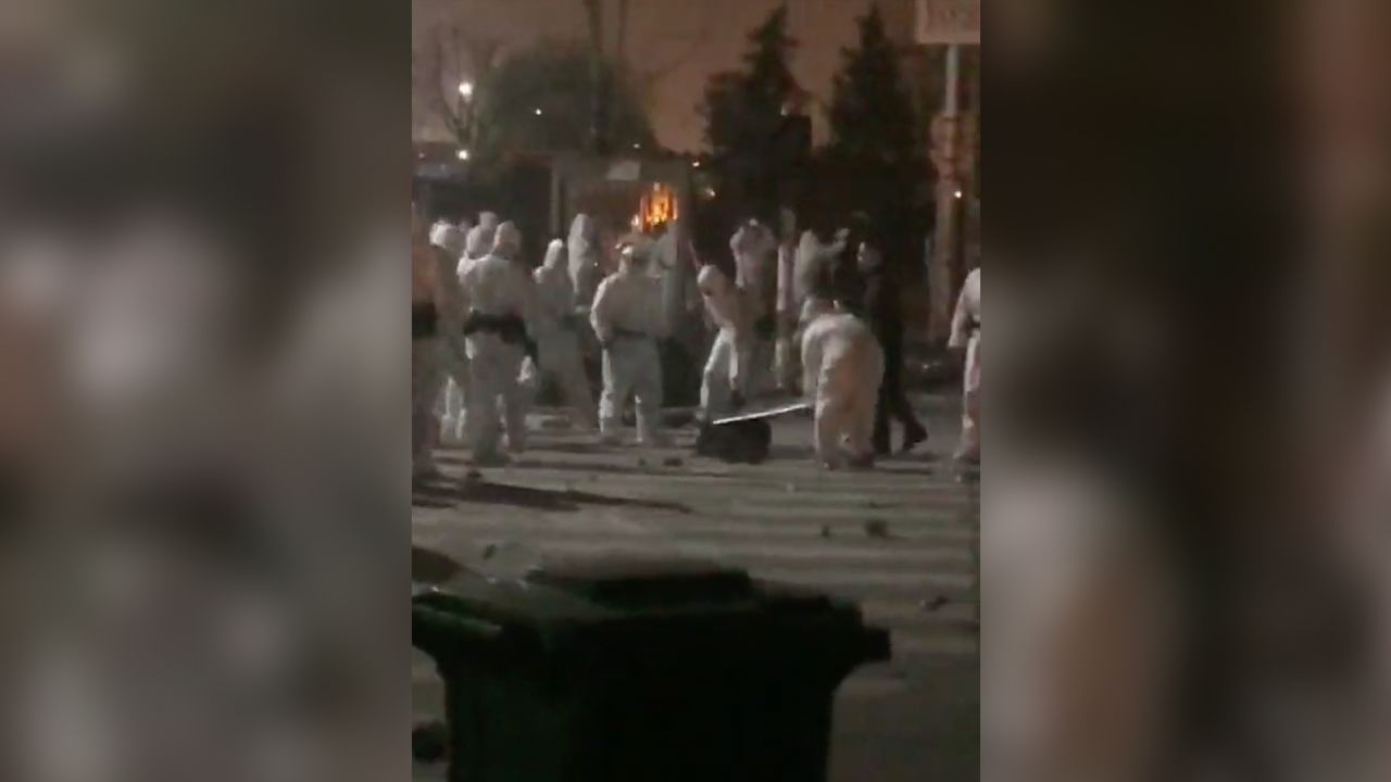 Un grupo de agentes de seguridad vestidos con trajes para materiales peligrosos patearon y golpearon a un trabajador que yacía en el suelo.