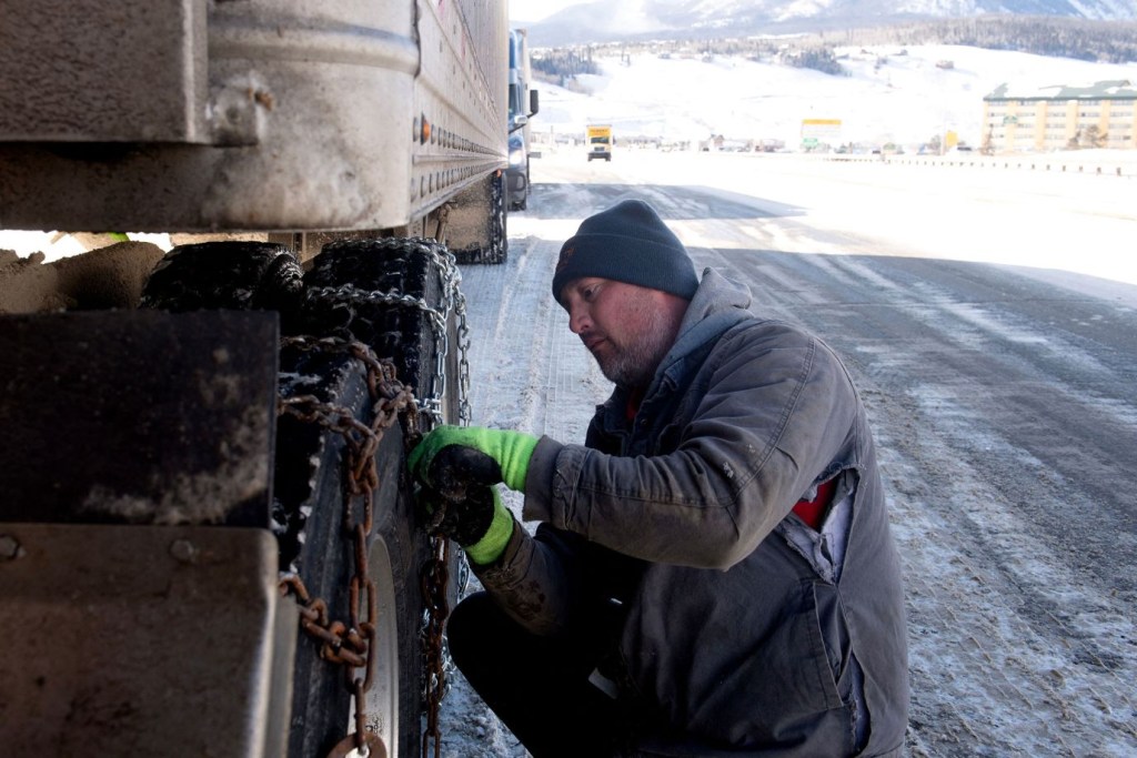 Robert Arnold coloca cadenas en las llantas de su semirremolque mientras espera a que se reabra el carril este de la I-70 en Silverthorne, Colorado, el 22 de diciembre. (Crédito: Jason Connolly/AFP/Getty Images)