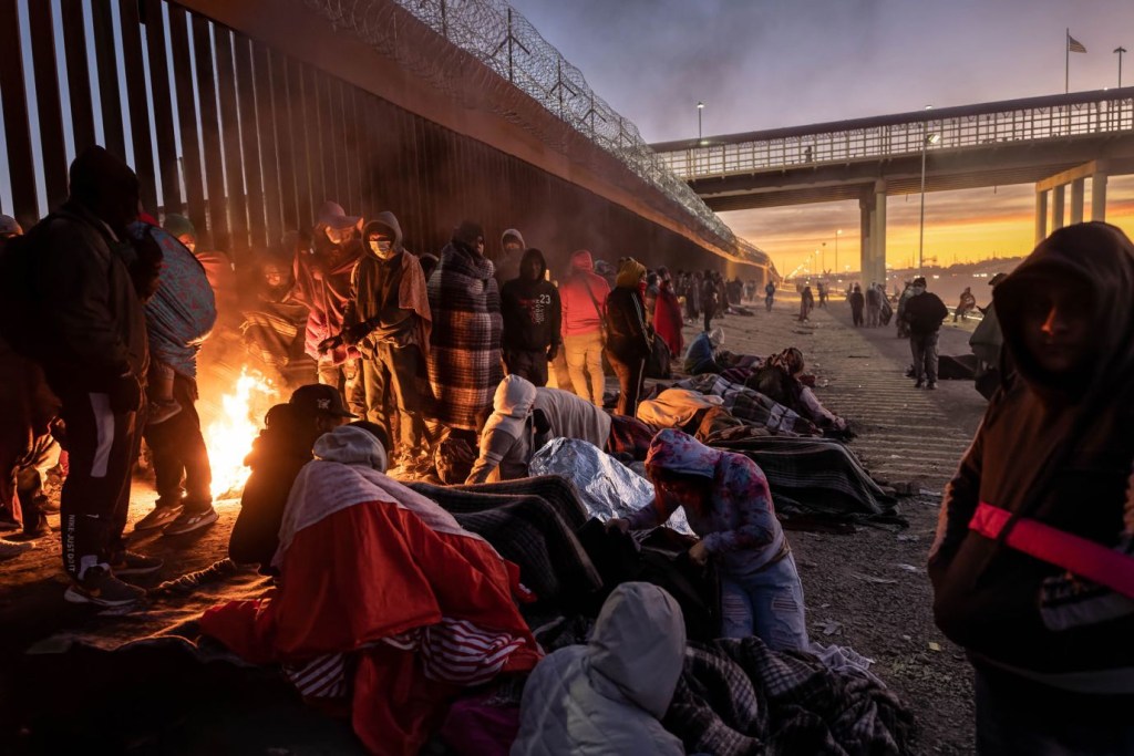 Migrantes se calientan junto a una fogata al lado de la valla fronteriza entre Estados Unidos y México, el 22 de diciembre en El Paso, Texas. (Crédito: John Moore/Getty Images)