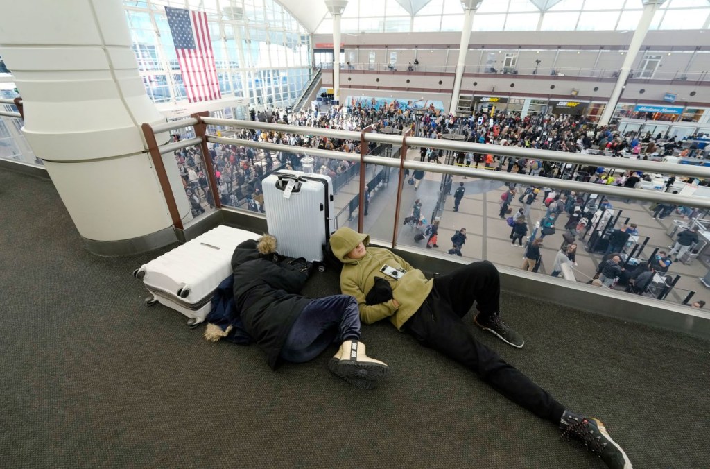 Una pareja de viajeros duerme mientras las filas de gente pasan por un control de seguridad en el Aeropuerto Internacional de Denver. (Crédito: David Zalubowski/AP)
