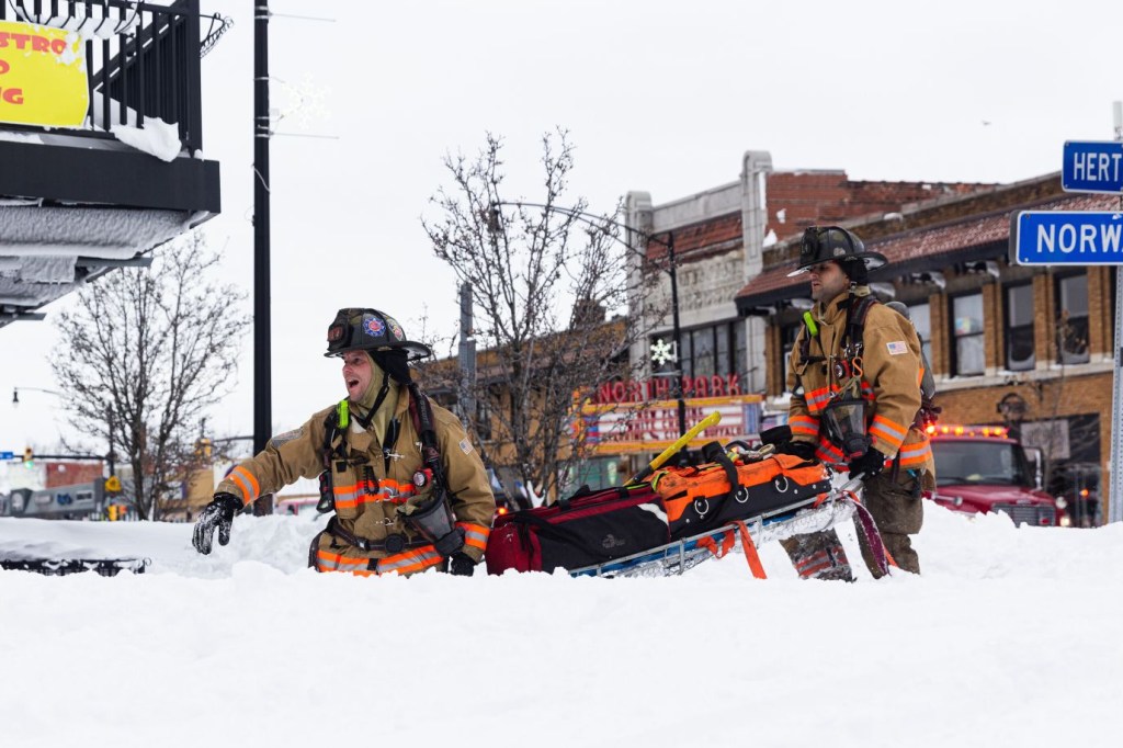 Bomberos portan equipos de rescate mientras responden a un incendio en una calle cubierta de nieve el día de Navidad en Buffalo. (Crédito: Jalen Wright/The New York Times/Redux)