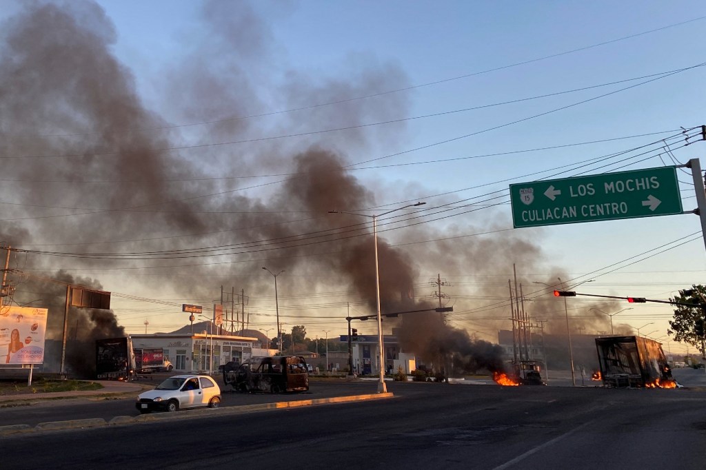 Vehículos con llamas se encuentran cruzando la calle en medio del violento trayecto tras la detención de Ovidio Guzmán.  (Crédito: MARCOS VIZCARRA/AFP vía Getty Images)