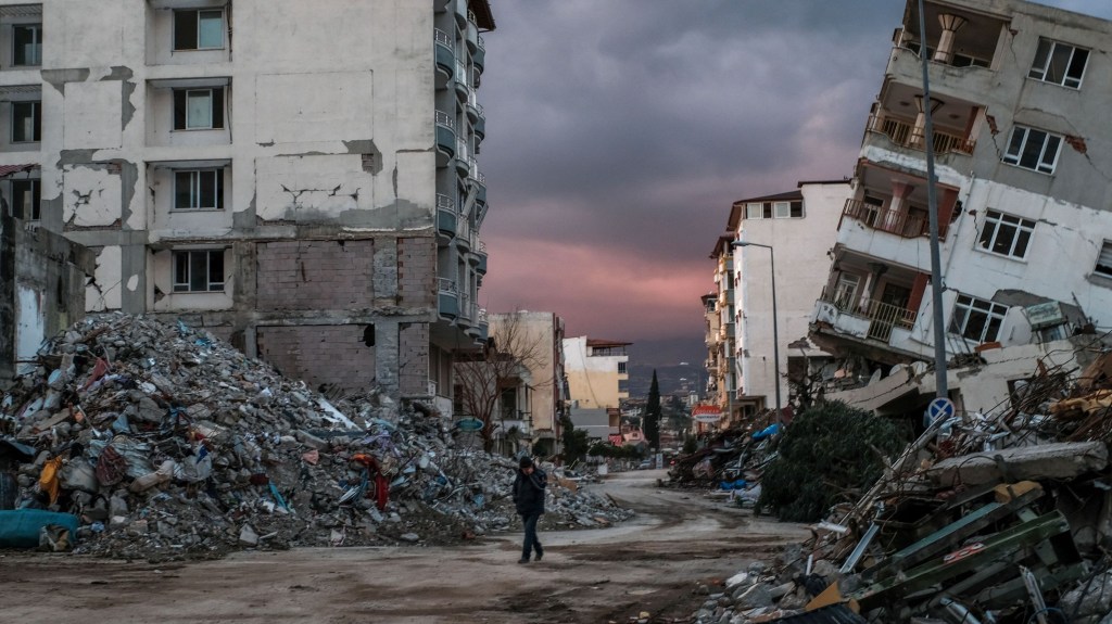 Un hombre camina entre edificios derrumbados, un día después de que un sismo de magnitud 6,4 sacudiera la región, en la ciudad costera de Samandag, ubicada en la provincia de Hatay, el 21 de febrero de 2023. (Crédito: BULENT KILIC/AFP vía Getty Images)