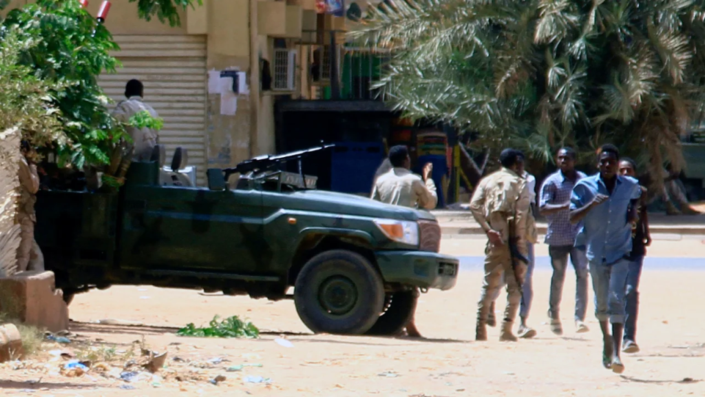 Varias personas pasan junto a un vehículo militar en Jartum el 15 de abril de 2023, en medio de los enfrentamientos registrados en la ciudad. Los paramilitares de Sudán dijeron que tenían el control de varios lugares clave tras los enfrentamientos con el ejército regular el 15 de abril, incluido el palacio presidencial en el centro de Jartum. (Crédito: -/AFP via Getty Images)