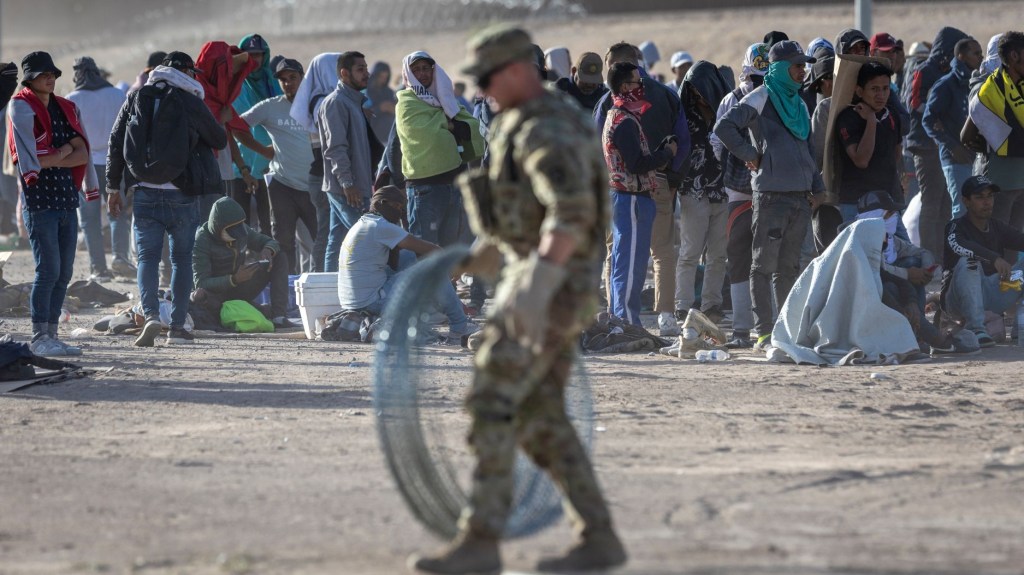 Migrantes observan mientras un soldado de la Guardia Nacional de Texas se prepara para desenrollar alambre de púas alrededor de un campamento improvisado de migrantes ubicado entre el Río Grande y la valla fronteriza entre Estados Unidos y México el 10 de mayo de 2023 en El Paso, Texas. (Foto: John Moore/Getty Images)