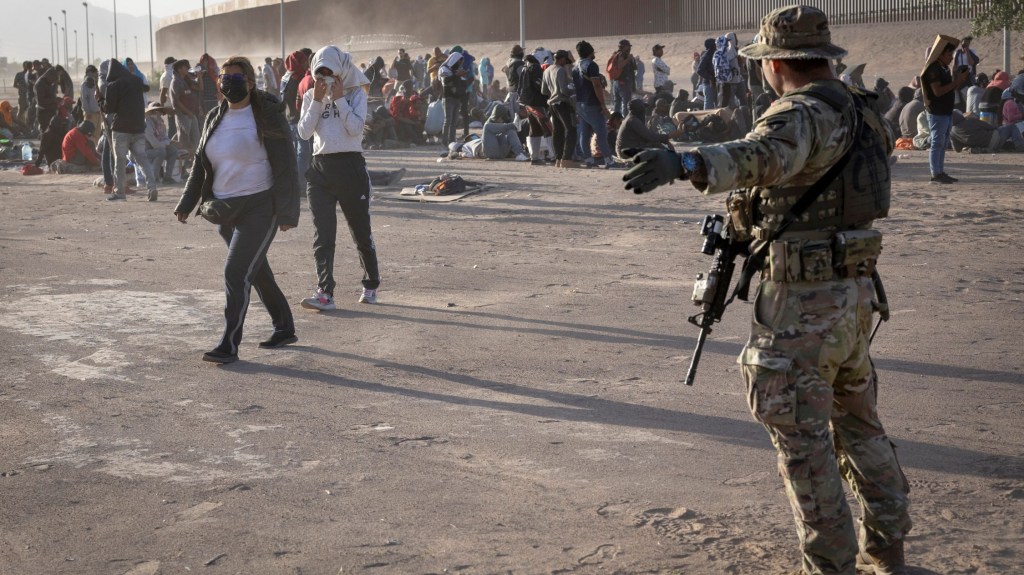 Un soldado de la Guardia Nacional de Texas orienta a los migrantes durante una tormenta de polvo en un campamento improvisado situado entre el Río Grande y la valla fronteriza entre Estados Unidos y México el 10 de mayo de 2023 en El Paso, Texas. (Crédito: John Moore/Getty Images)