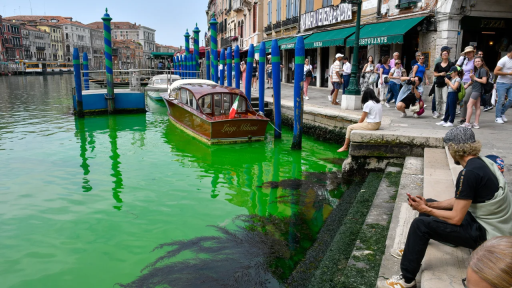 La gente observa el histórico Gran Canal de Venecia mientras una mancha de líquido verde fluorescente se extiende en él. (Foto: Luigii Costantini/AP)