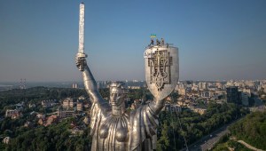 Los trabajadores ondean la bandera ucraniana tras terminar de instalar el escudo de Ucrania en el escudo del Monumento a la Patria, de 62 metros de altura, en Kiev, Ucrania, el 6 de agosto. (Foto: Roman Pilipey/AFP/Getty Images)