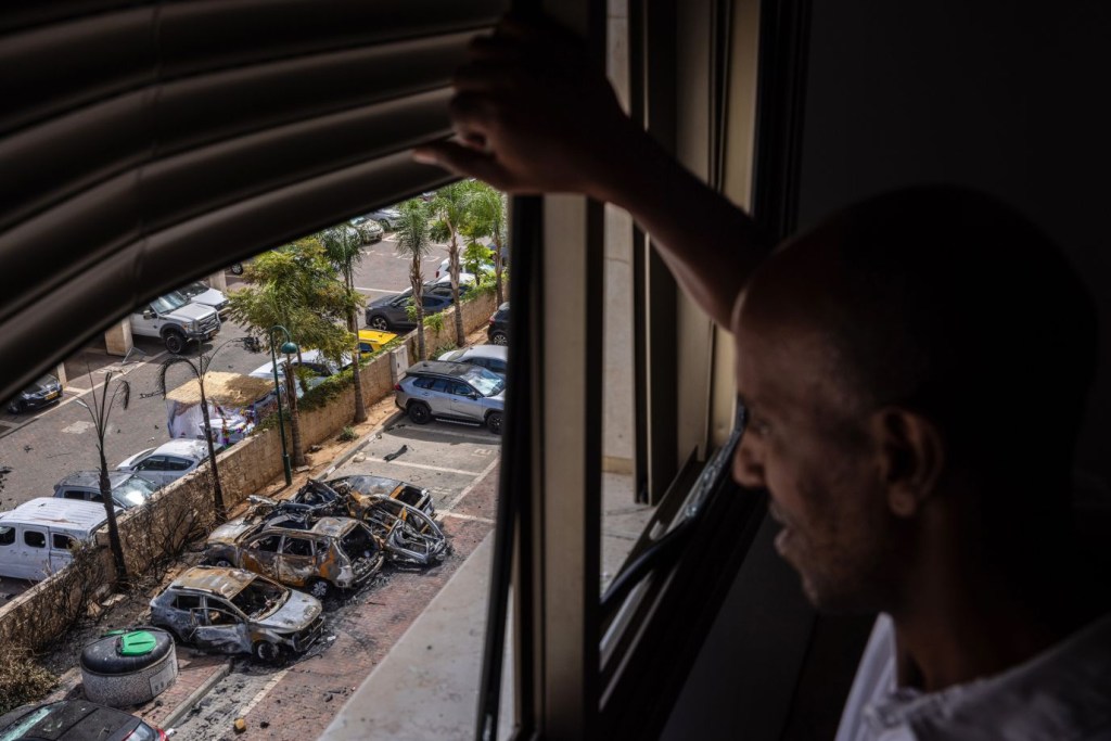 Desde la ventana del apartamento de su familia, un hombre observa los daños causados por un cohete que impactó en un aparcamiento en Ashkelon el 7 de octubre. (Crédito: Tamir Kalifa/The New York Times/Redux)