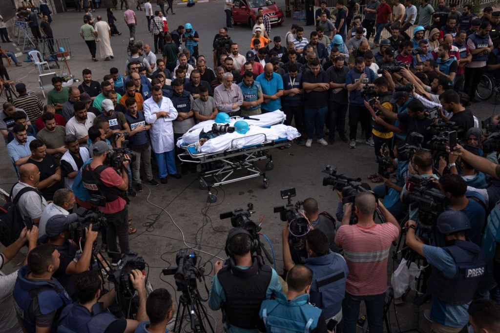 Varias personas se reúnen en torno a los cadáveres de dos reporteros palestinos, Mohammed Soboh y Said al-Tawil, que murieron en un ataque aéreo israelí en la ciudad de Gaza el 10 de octubre. (Crédito: Fatima Shbair/AP)