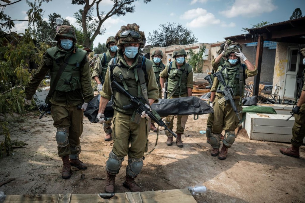 Soldados israelíes llevan un cadáver el 10 de octubre en Kfar Azza, pueblo israelí situado al otro lado de la frontera con Gaza. Militantes de Hamas llevaron a cabo una "masacre" en Kfar Aza durante sus ataques del fin de semana, según informaron las Fuerzas de Defensa de Israel a CNN. (Crédito: Sergey Ponomarev/The New York Times/Redux)