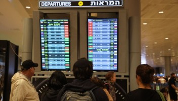 Los pasajeros miran un tablero de salidas en el aeropuerto Ben Gurion cerca de Tel Aviv, Israel, el 7 de octubre de 2023, mientras los vuelos se cancelan debido a los ataques sorpresa de Hamas. (Crédito: GIL COHEN-MAGEN/AFP vía Getty Images)