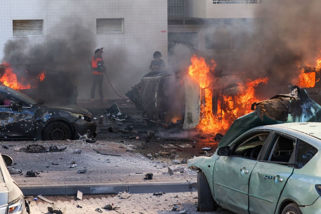 Varias personas intentan apagar el fuego de los coches tras un ataque con cohetes en Ashkelon, en el sur de Israel, el 7 de octubre de 2023. (Crédito: Ahmad Gharabli/AFP/Getty Images)