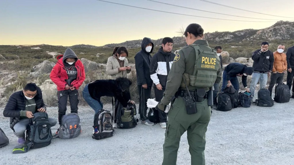 Un agente de la Patrulla Fronteriza de Estados Unidos habla con migrantes mientras esperan su procesamiento en la frontera entre Estados Unidos y México en el condado de San Diego. (Crédito: Norma Galeana/CNN)
