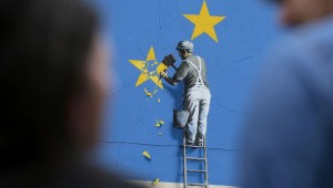 Gente cerca de un mural pintado por el artista británico de graffiti Banksy, que muestra a un trabajador cortando una de las estrellas de una bandera con temática de la Unión Europea, en 2017. (Crédito: Daniel Leal/AFP/Getty Images)